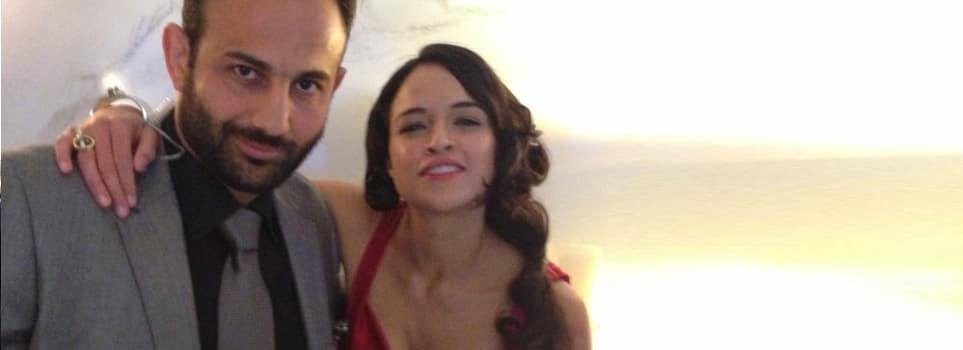 Roman Mitichyan in a grey suit beside a woman in a red dress at a party in Furious Seven
